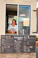 Sorrento's Coffee owner smiling from the drive-thru window, with the menu board below