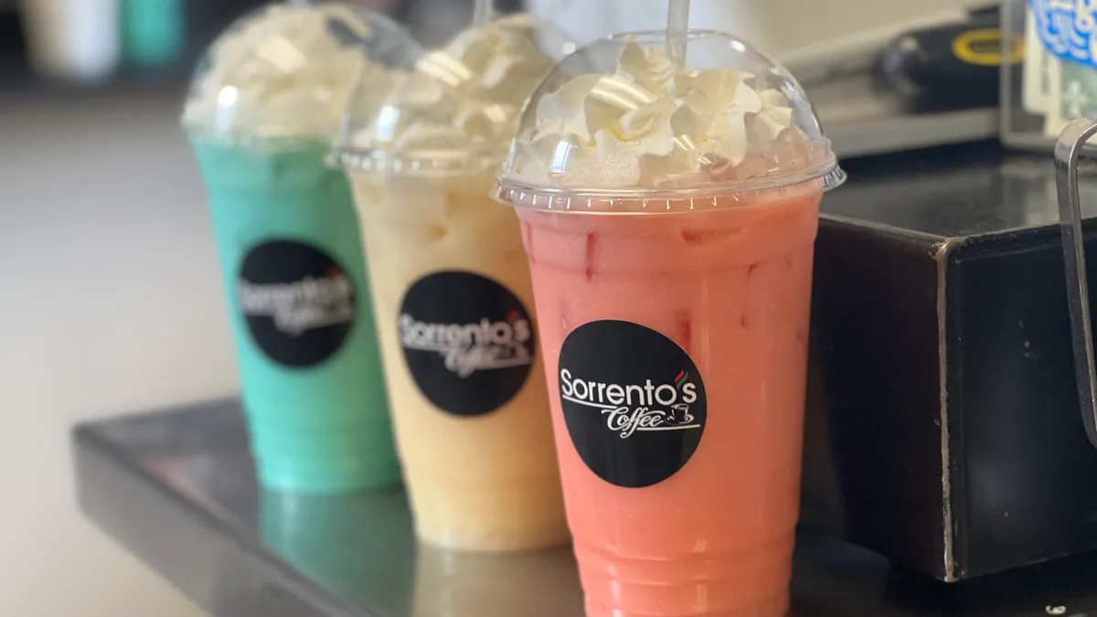 Three whipped-cream-topped Sorrento's Coffee drinks in green, yellow, and pink