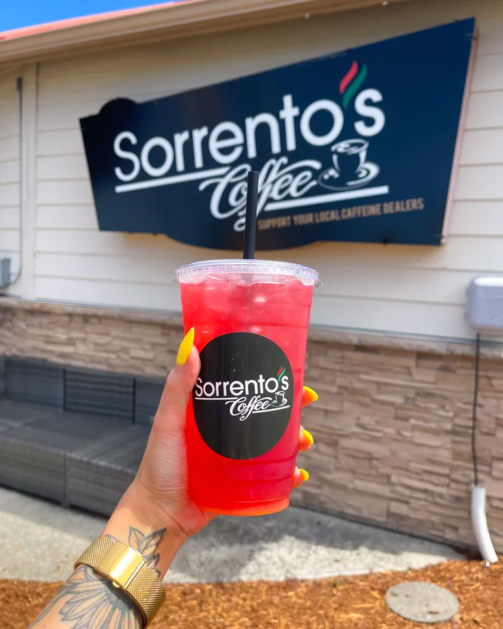 A hand holding a bright red Sorrento's Coffee drink in front of the storefront sign